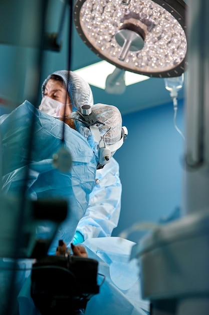 surgeon performing cosmetic surgery in hospital operating room surgeon in mask wearing loupes during medical procadure breast augmentation