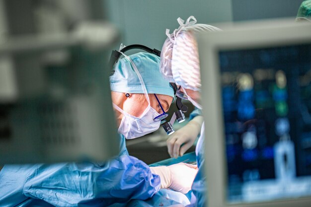 Surgeon performing surgery in hospital operating room. Surgeon in mask wearing loupes during medical procadure.