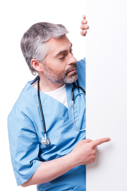 Surgeon pointing copy space. Confident mature surgeon pointing copy space while standing isolated on white