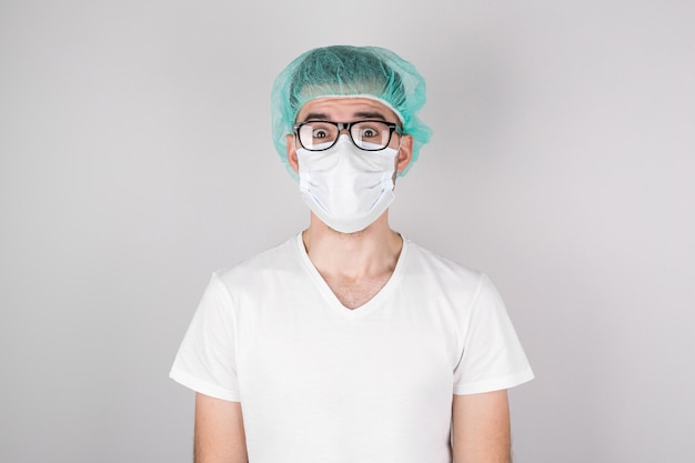 A surgeon in a white medical mask and a medical cap stands on a white background