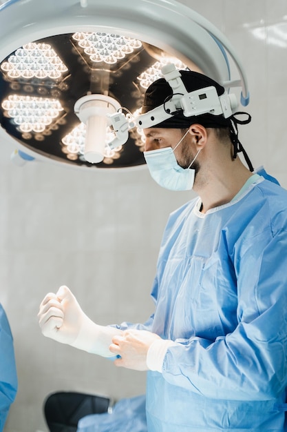 Surgeon with headlight is preparing for surgery in medical clinic Male surgeon puts on surgical gloves and disinfects before operation