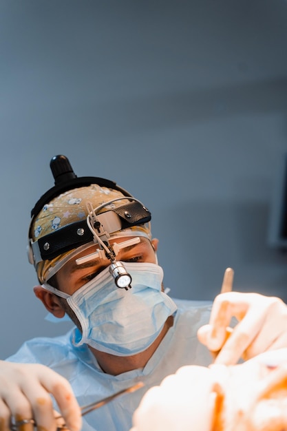 ヘッドライトを持つ外科医は手術室で働いています。目の領域を変更するための眼瞼形成術整形手術の外科医は手術用ナイフで切開を行っています。