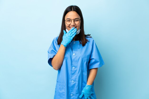 Foto donna del chirurgo sopra la parete blu felice e sorridente che copre la bocca con la mano