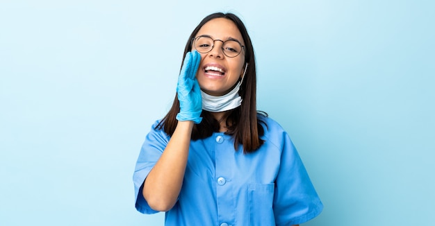 Surgeon woman over blue wall shouting with mouth wide open