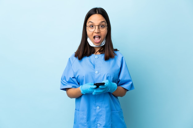 Surgeon woman over blue wall surprised and sending a message