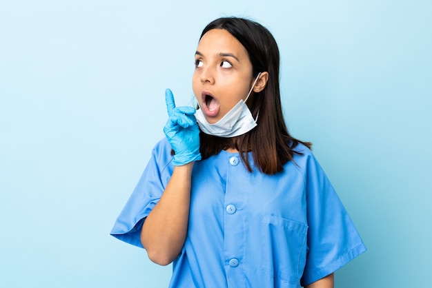 Женщина хирурга над голубой стеной думая идея указывая палец вверх