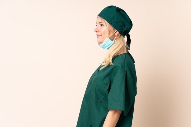 Surgeon woman in green uniform over isolated background looking to the side