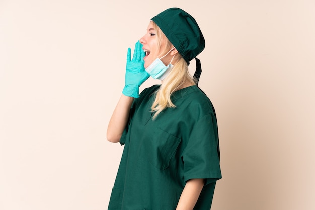 Surgeon woman in green uniform over isolated wall shouting with mouth wide open