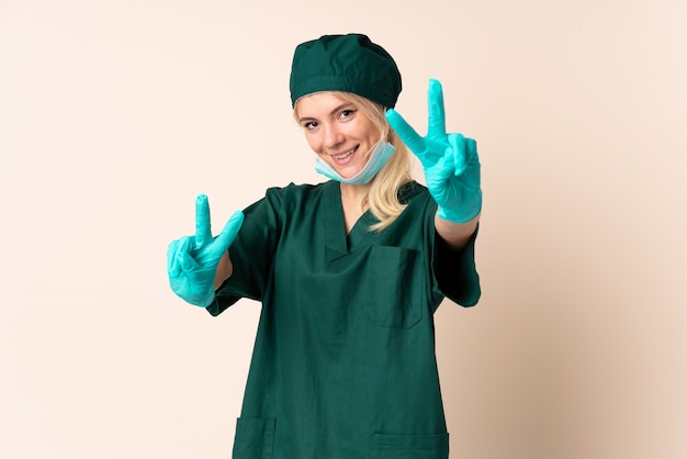 Surgeon woman in green uniform over isolated wall smiling and showing victory sign