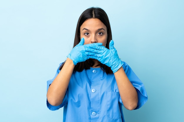 Surgeon woman over isolated blue wall covering mouth with hands