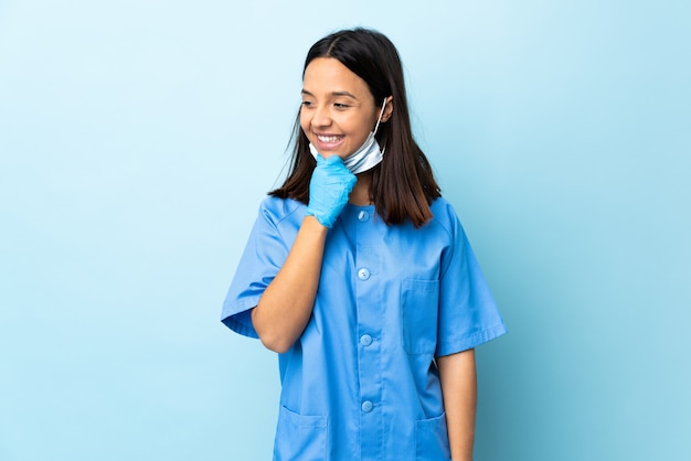 Surgeon woman over isolated blue wall looking to the side and smiling