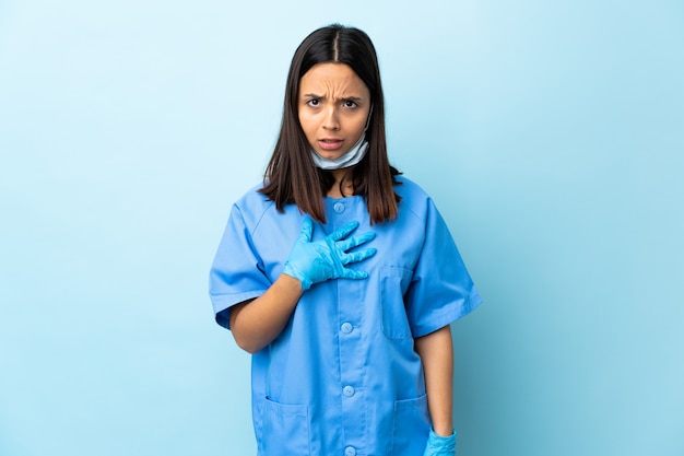 Surgeon woman over isolated blue wall pointing to oneself