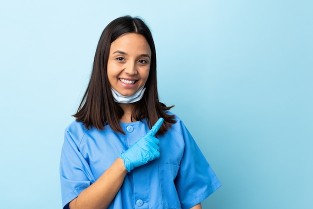 Женщина хирург над изолированной синей стеной, указывая на сторону, чтобы представить продукт