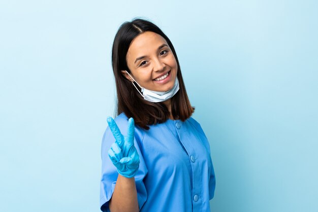 Surgeon woman over isolated blue wall smiling and showing victory sign