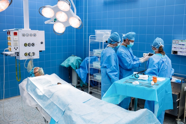 Surgeons using digital tablet and patient lying on operation bed