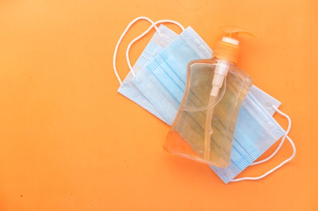 Surgical masks and hand sanitizer on orange background