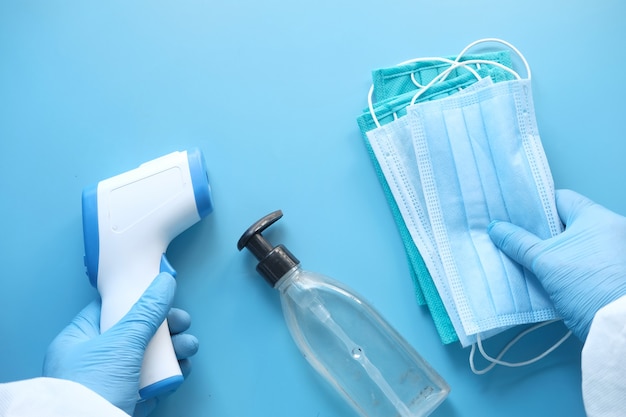 Surgical masks, thermometer and hand sanitizer on blue background