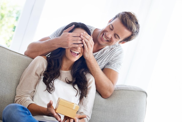 Surprise cover eyes and couple in house with gift love and playful in marriage with anniversary in home Man hands and woman face for present in relationship together and celebrate in living room