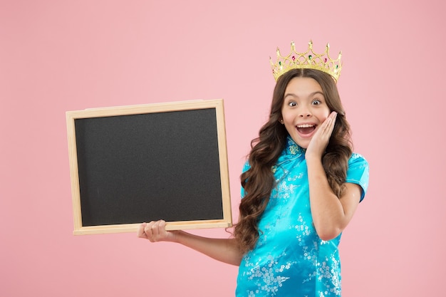 Surprise prom night. Prom queen hold school blackboard. Small child wear prom crown. Coronation party. Holiday celebration. Pride and glory. Prestige and fame. Prom information, copy space.