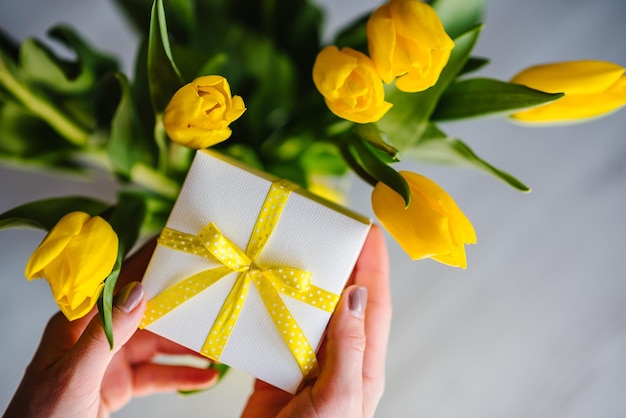 Surprise Woman hand hold gift box on yellow tulips background Space for message Greeting card Holiday greeting card for Valentine's Women's Mother's Day Easter Happy Birthday