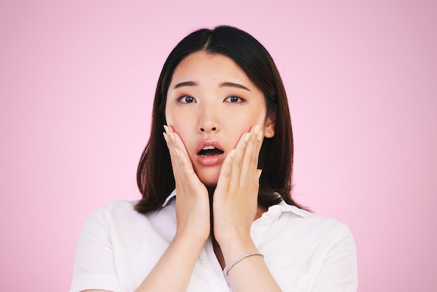 Surprise wow and hands on woman face in studio with anxiety for fake news drama or secret on pink background Omg portrait and Japanese female model shocked by gossip announcement or emoji info