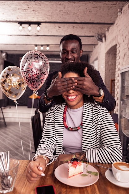 Surprise for you. Positive joyful man standing behind a woman while preparing a surprise for her