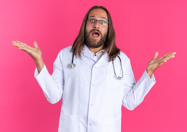 Surprised adult male doctor wearing medical robe and stethoscope with glasses showing empty hands 