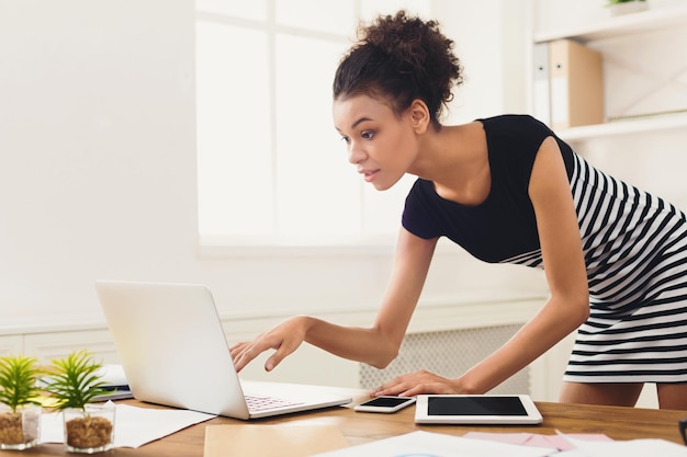 Surprised african-american businesswoman in modern office. Woman working on laptop at office, copy space