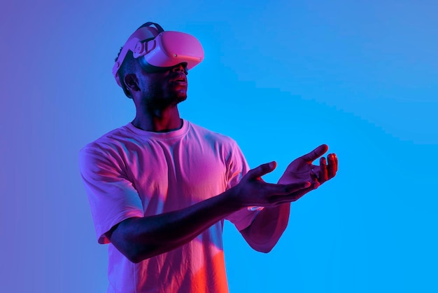 surprised african american man in virtual reality glasses holding empty hands in neon lighting