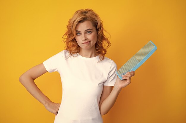 Surprised amazed girl combing hair Redhead woman with a comb isolated on yellow background Woman