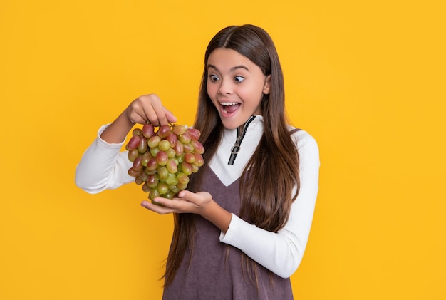 Surprised amazed girl hold fresh grapes fruit on yellow background