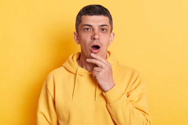 Surprised amazed man wearing casual style hoodie posing isolated over yellow background looking at camera with big eyes and open mouth shocked by news