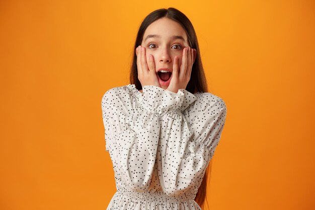 Surprised amazed teen girl against yellow background in studio