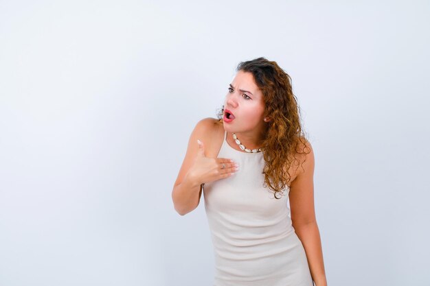 Surprised and angry girl is looking left by showing herself with hand on white background