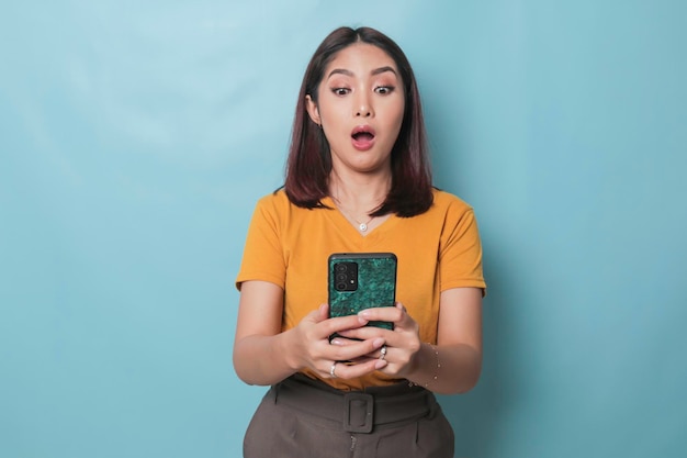 Surprised Asian woman looking at her smartphone over blue background