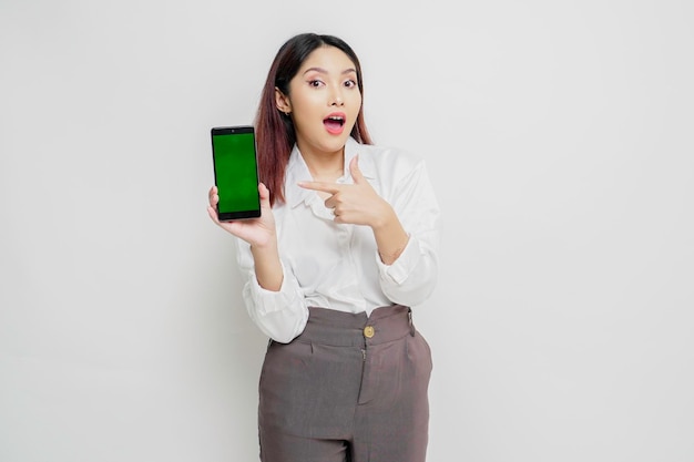 흰색 배경에 격리된 스마트폰에 복사 공간을 보여주는 흰색 셔츠를 입은 놀란 아시아 여성