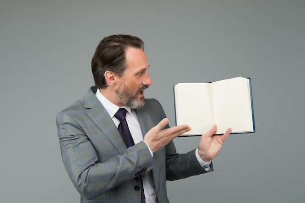 L'uomo barbuto sorpreso in tailleur formale mostra il libro aperto per informazioni, copia spazio.