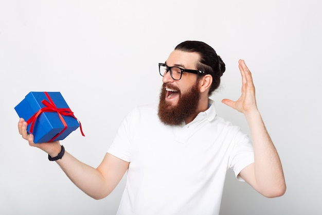 L'uomo barbuto sorpreso sta tenendo una confezione regalo su sfondo bianco.