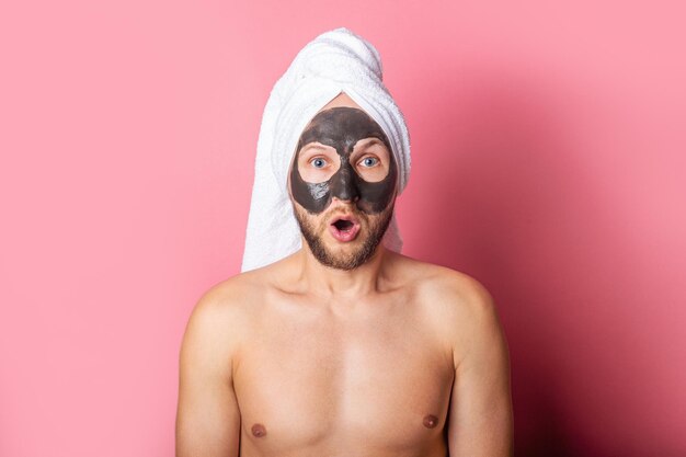 Surprised bearded young man with cosmetic mask on his face background Care cleaning