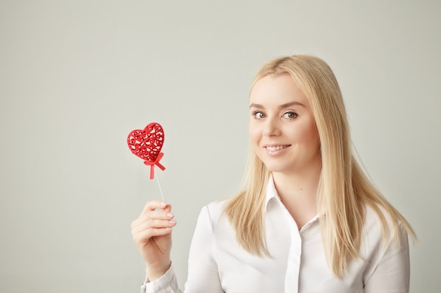 Modello di moda sorpreso della bella ragazza con il cuore di san valentino in mano sul muro bianco