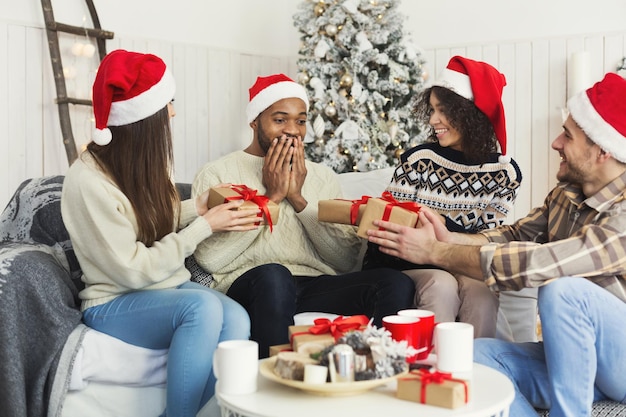 Uomo di colore sorpreso che riceve regali dagli amici, festeggia il natale a casa insieme, copia spazio