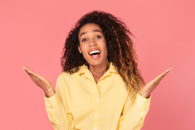 Surprised black woman with raised hands on pink background