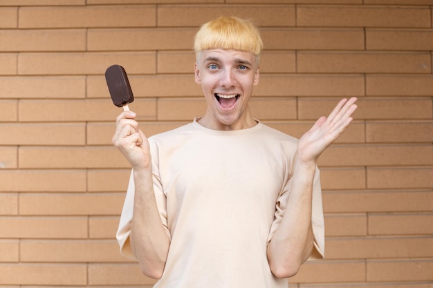 Surprised blond Caucasian guy holding an ice cream stick in his hand looking at the camera