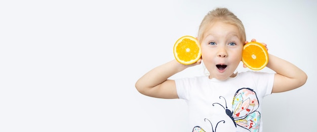 Surprised blonde child girl holding two cut halves of an orange on a white background Banner