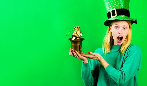 Surprised blonde girl in green hat with pot of gold saint patricks day irish traditions