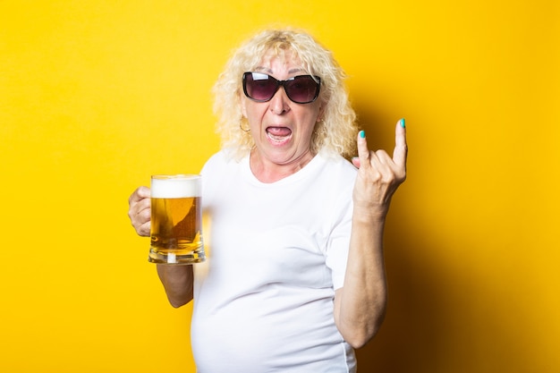 Foto donna anziana bionda sorpresa che tiene un bicchiere di birra e mostra una capra a bilanciere