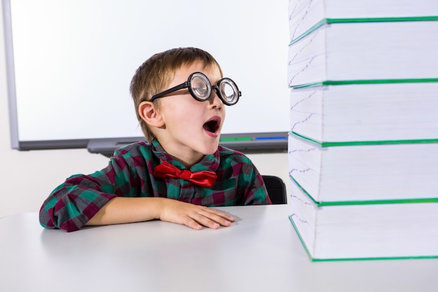 Surprised boy by stacked books in classroom