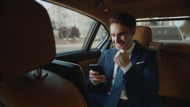 Surprised businessman getting good news on smartphone in interior of modern car