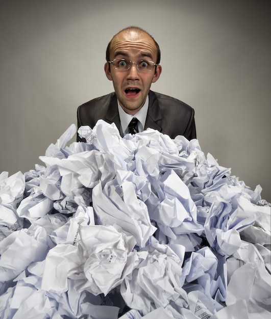 Surprised businessman reaches out from crumpled papers