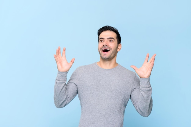 Surprised Caucasian man gasping and raising hands up isolated on light blue background